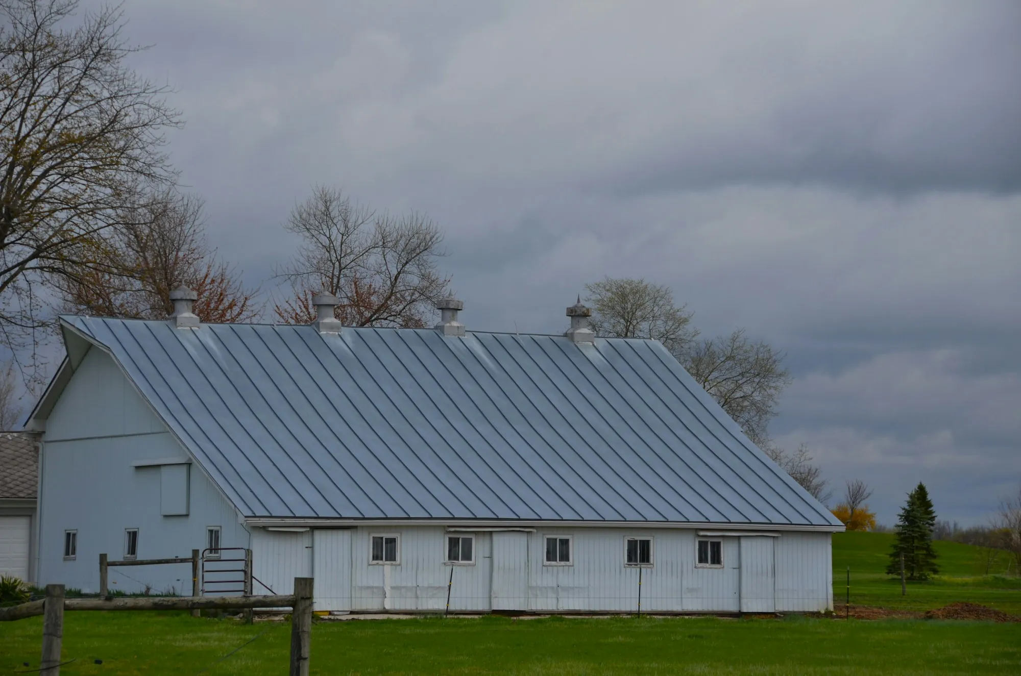 White barn with a standing seam metal roof under gray skies
