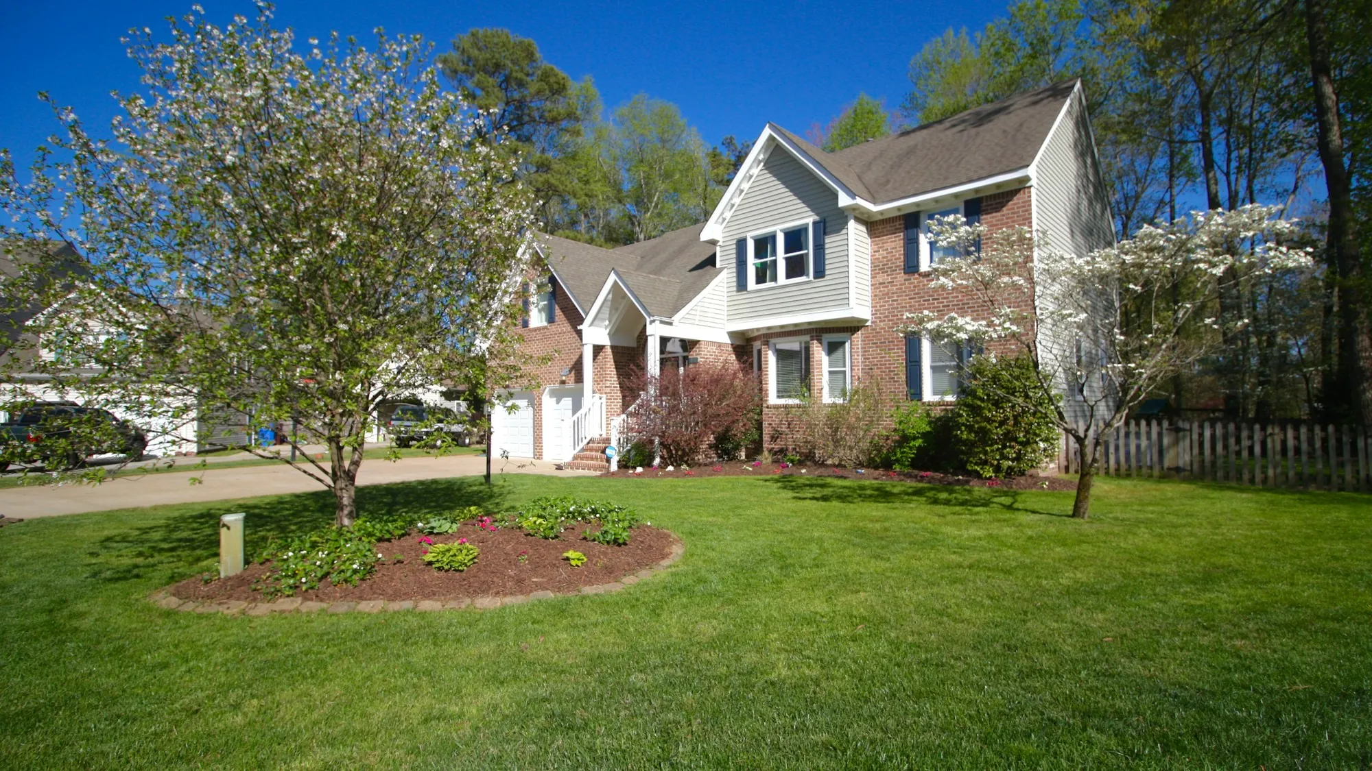 Brick and siding home with a multi-level shingle roof and spring garden