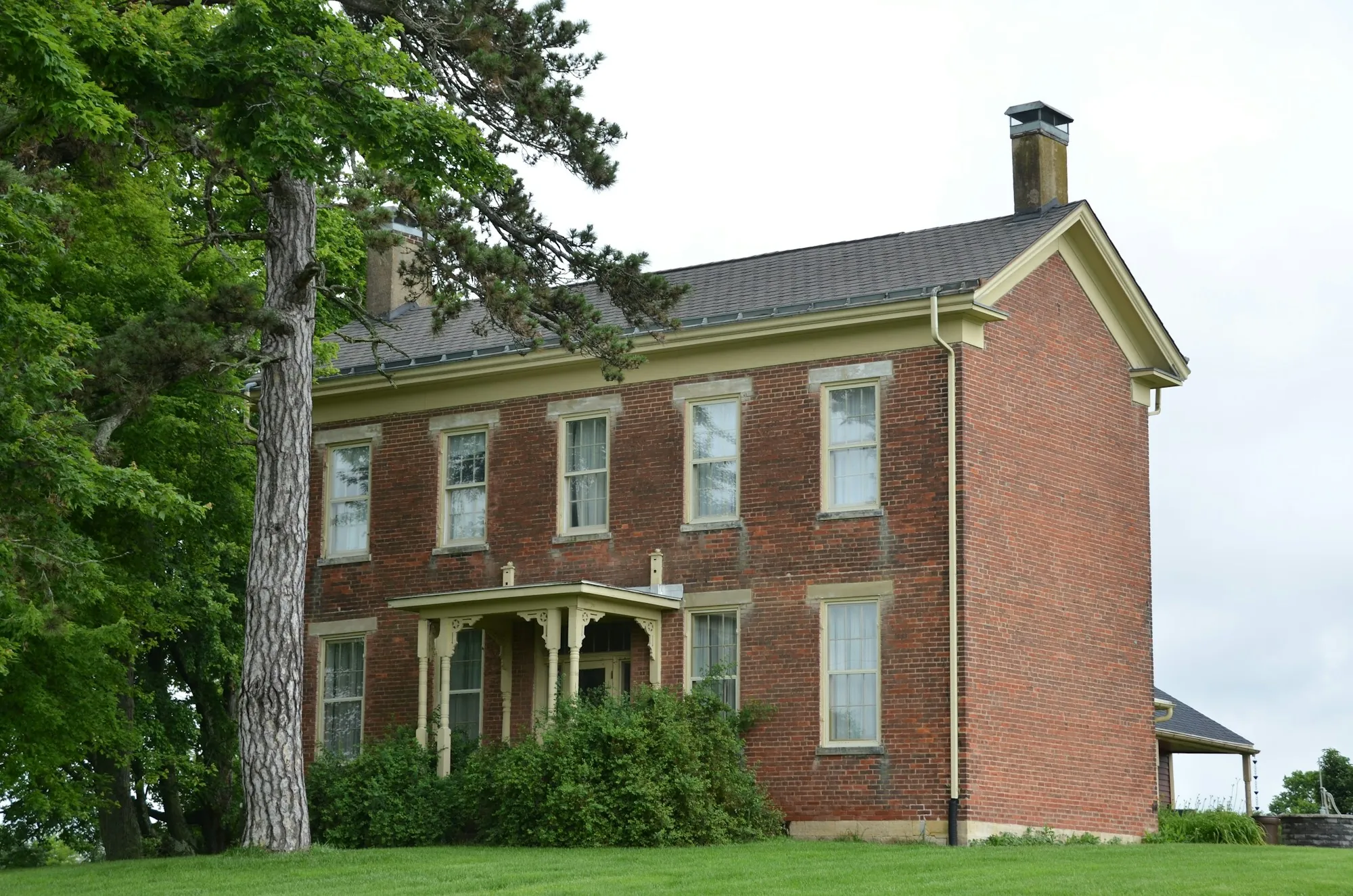 Two-story brick farmhouse among tall trees